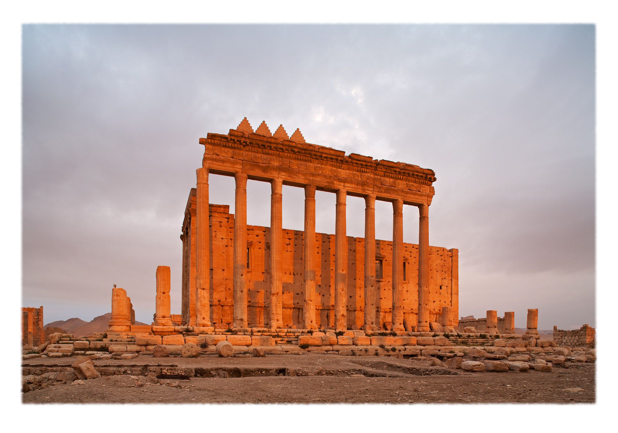 The warm glow of first light on the rear facade of the elevated Temple, featuring stepped merlons (<i>shurafat</i>) and Corinthian columns and entablature.